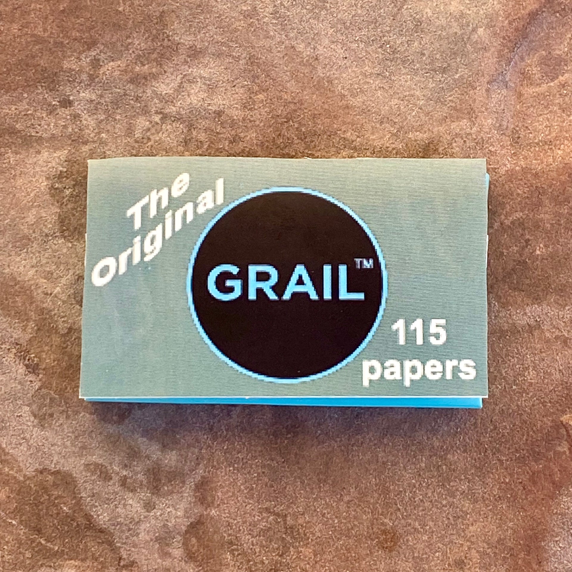 Closed box of Grail™ rolling papers labeled “The Original – 115 papers,” placed on a textured brown stone surface